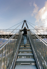 female hiker climbing up metal stairs that  lead up to an impressive lookout and viewpoint platform in the Grisons near Flims in Switzerland under a blue sky with white clouds