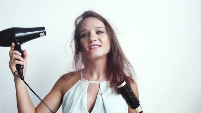 Beautiful young brunette woman using hairdryer dries hair combing on a white background. slow motion. 3840x2160