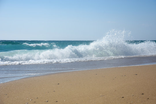 Big breaking wave on a sandy beach. Beautiful sandy beach with big sea waves on sunny summer day