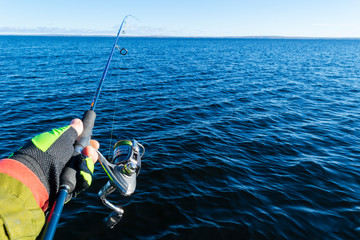 Fishing on the lake. Hands of fisherman with fishing rod. Macro shot. Fishing rod and hands of fisherman over lake water. Spinning rod. Fishing tackle