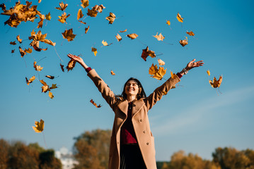 Beautiful young happy girl with a bright red-yellow autumn leaf in the park