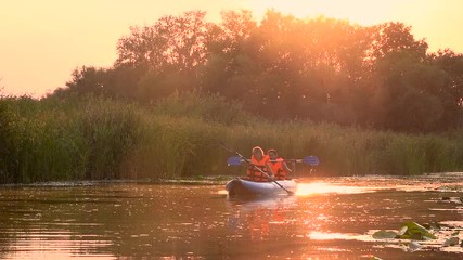 Pair of people in kayaks floats on a river in a sunset. Slow motion