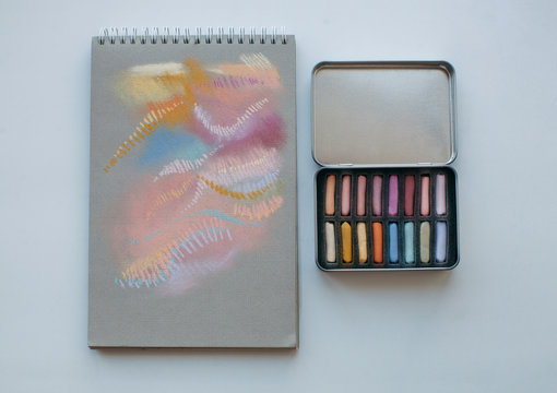 Metal box with assorted soft pastels and notebook with abstract drawing made with it