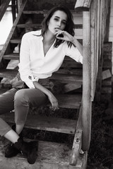 Fashion portrait of a beautiful girl near on the steps of a wooden house by the lake. Posing and resting at sunset. Emotional portrait of a girl