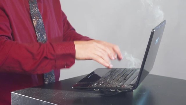 Man hands and fingers on broken laptop computer. Smoke in room.