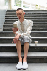 Young androgynous homosexual LGTB businessman sitting on stairs while using phone