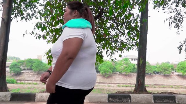 Slow motion of overweight woman running on the street and taking a break while wiping her sweat