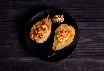 Two halves baked with cottage cheese, nuts and dried apricots pears on a black plate. close-up