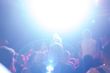 a crowd of people illuminated by floodlights, stand with their hands up and listen to a musical rock concert, blurred background