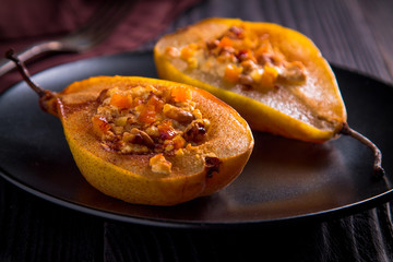 Two halves baked with cottage cheese, nuts and dried apricots pears on a black plate. close-up