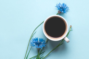 Spring background. Cornflowers and a cup of hot coffee on a blue background.