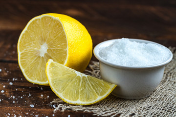 Lemon acid in a white, small plate, a slice of lemon and a juicy lemon on a wooden background....