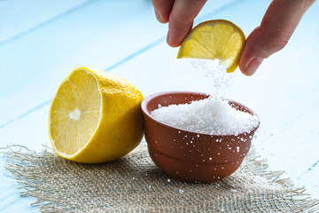 Lemon acid in a brown, small plate, a slice of lemon in hands and a juicy lemon on a wooden background. Citric acid. - obrazy, fototapety, plakaty