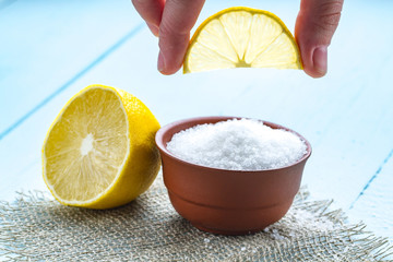 Lemon acid in a brown, small plate, a slice of lemon in hands and a juicy lemon on a wooden...