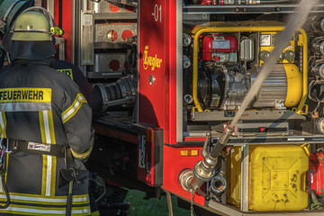 The fire brigade practices the use of water cannons. On the protective suit is in German: Feuerwehr. Gandesbergen, Germany / 14 May 2018