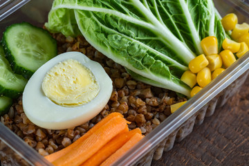 Healthy meal in a plastic container. Snack in the office, at work. Lunch box of cucumbers, buckwheat, carrots, eggs, lettuce and canned corn. Nutrition and healthy food concept