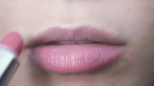 Woman doing make up lips paints pink lipstick on top her lips