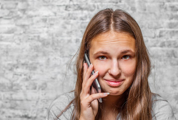 portrait of young teenager brunette girl with long hair using mobile phone on gray wall background