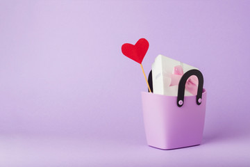 Small plastic bag for shopping, gift boxes, heart on a stick, purple background. Concept of...