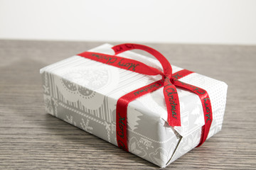 Christmas gift with white paper and a red ribbon on a wood table