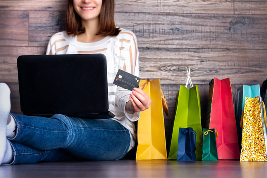 Woman female adult smiling buying making payment on fashion cloth internet online store shop by credit debit card with laptop during black friday holiday with colorful shopping bags at home.