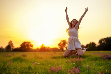 Happy cheerful girl is jumping on nature over the summer sunset background