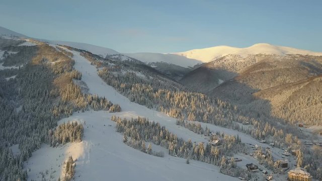 Flight over a village in Carpathian mountains. Bird's eye view of snow-covered houses in mountains. Rural landscape in winter. Carpathian village in the snow from a height.