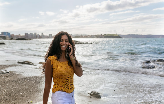Young woman walking on the beach while talking on the phone