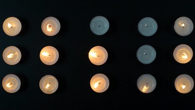 Footage of fifteen candles burning and fading by the wind on a black background.