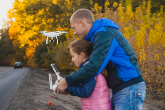 father and daughter with flying drone in the autumn park. Man with remote controller in his hands taking aerial photos and videos