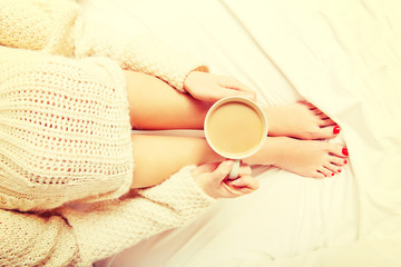 Young woman sitting in bed with a cup of coffee