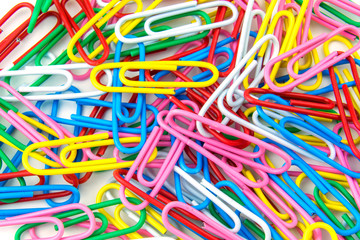 Multi-colored paper clips in bulk lie on a white background. Close up