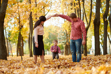 Parents and child are walking in autumn city park. Bright yellow trees.