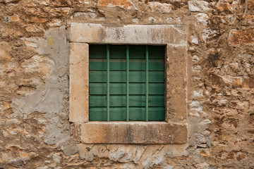 Fototapeta na wymiar Small stone window closed with green wooden planks and green metal bars. Old style window.