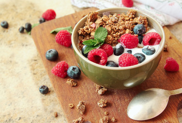 Healthy breakfast. Chocolate granola, muesli with yogurt and fresh berries in a bowl on wooden background.
