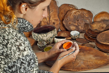 The girl paints pottery. Handmade products on the table at home workshop. Ceramic products with drawings and patterns.