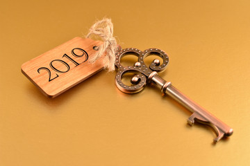 Key to the New Year 2019. Old key with wooden tag. Decorated key isolated on a golden background. Romantic key with wooden label. Golden New Year 2019