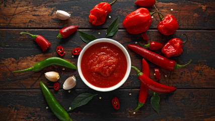 spicy hot sweet chili sauce with mix of chilli pepper, garlic and tomatoes on rustic wooden...