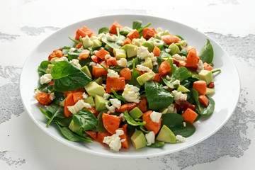 Avocado, roasted sweet potato, spinach, feta cheese healthy salad in white plate.