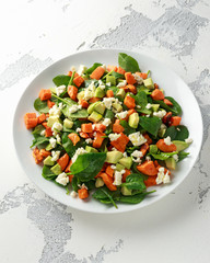 Avocado, roasted sweet potato, spinach, feta cheese healthy salad in white plate.