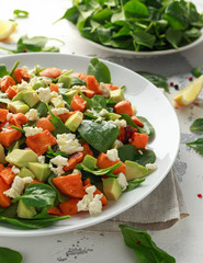 Avocado, roasted sweet potato, spinach, feta cheese healthy salad in white plate.