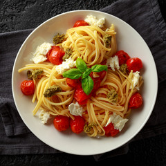 Pasta with green pesto sauce, roasted cherry tomatoes and mozzarella cheese in white plate on dark rustic background