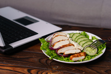 healthy lunch at workplace. diet, proper nutrition, balanced food. salad and chicken near laptop