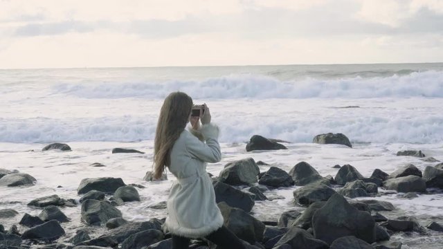 Girl photographer on the shore of the stormy sea makes pictures. Tourist traveler photographer making pictures ocean. Stormy sea with storm clouds. Snapshots of a trip to the sea.4k.30fps.