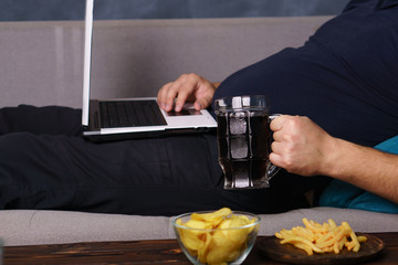overeating, sedentary lifestyle, bad habits, food addiction, eating disorders, depression. Lonely man watching series at laptop drink beer eat junk food