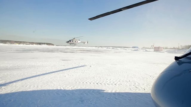 The helicopter sits on a snow-covered field. Helicopters of white color on the field. Another helicopter lands