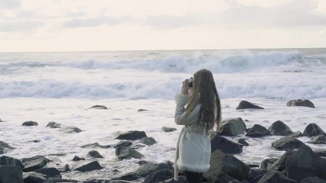 Girl photographer on the shore of the stormy sea makes pictures. Tourist traveler photographer making pictures ocean. Stormy sea with storm clouds. Snapshots of a trip to the sea.4k.30fps.