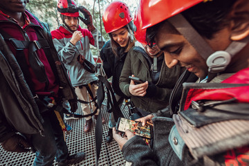 Friends share photos and videos on their phones during an outdoor zip line adventure