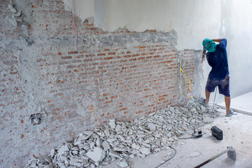 Portrait of worker using the drilling machine punching to the bricklayer wall at the house under...