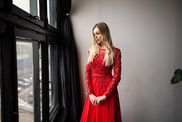 beautiful young girl in a red dress by the window